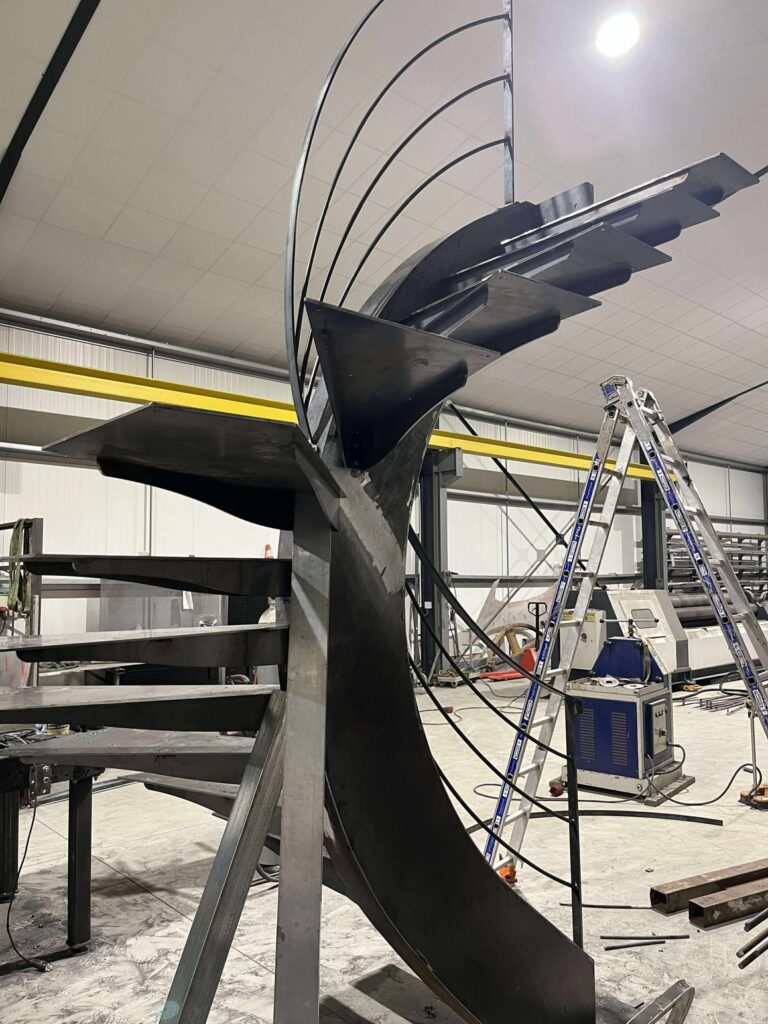 Fabrication d'un escalier hélicoïdal moderne en acier noir dans un atelier de métallerie industriel.