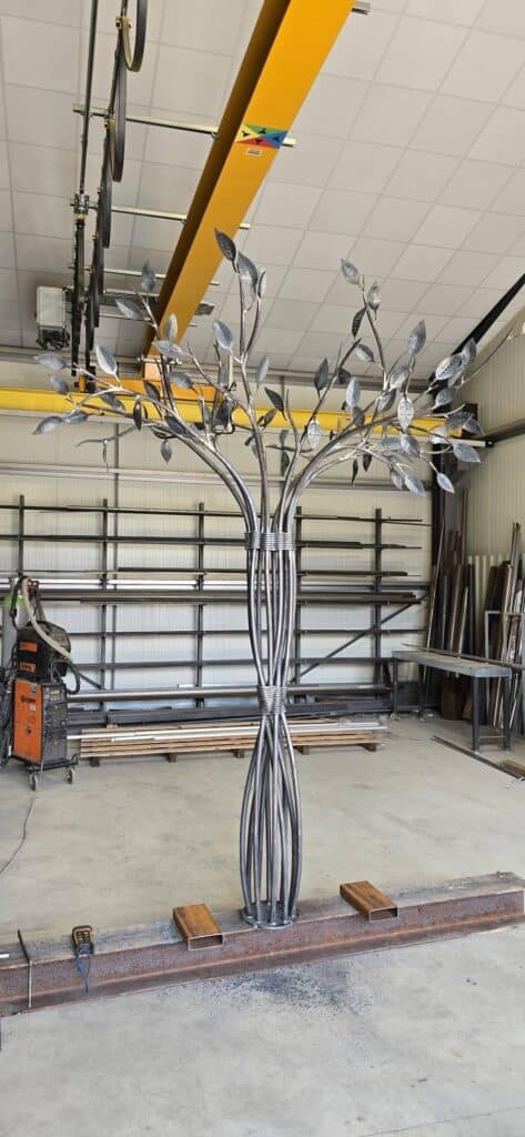 Sculpture d'arbre en acier forgé aux feuilles ciselées dans un atelier de ferronnerie industrielle.