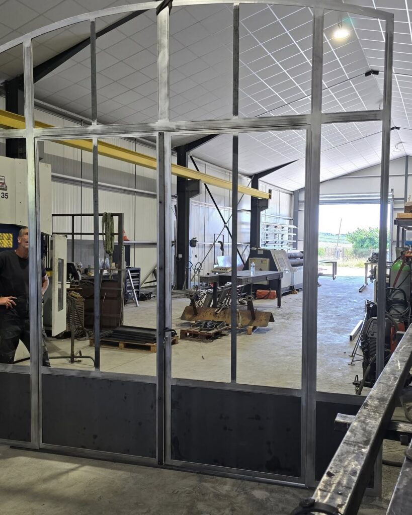 Verrière Industrielle en Acier : Fabrication sur Mesure Grande verrière industrielle en acier sur mesure dans un atelier de métallerie avec un artisan.