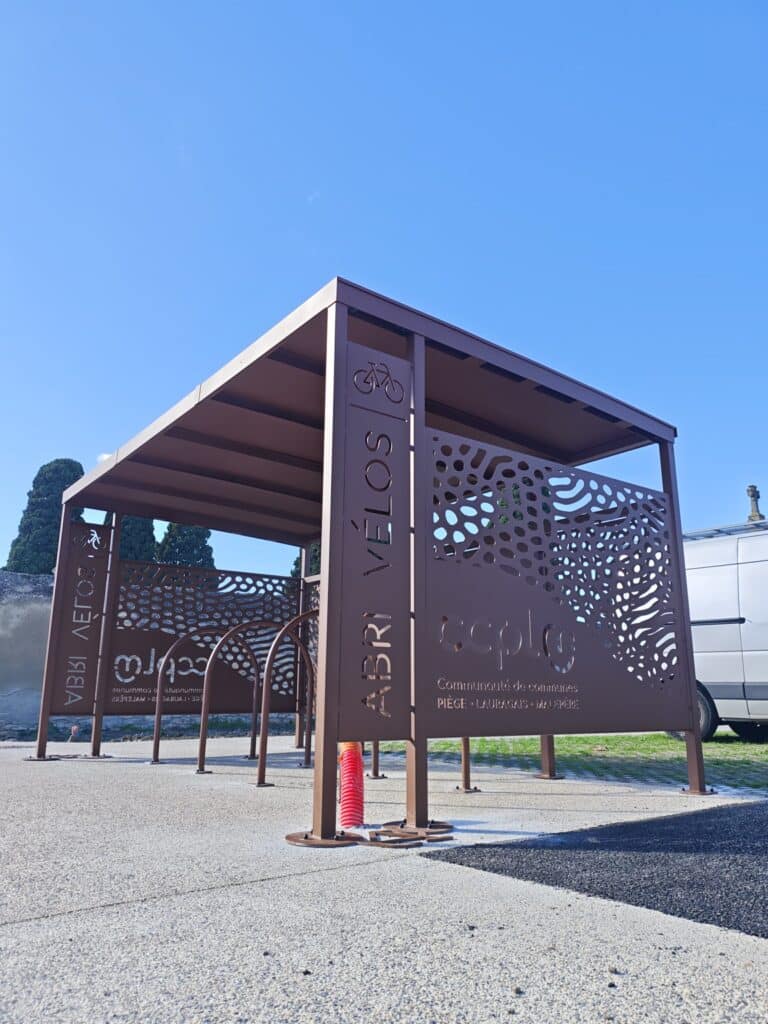 Abri vélos design CCPLM Piège Lauragais Malepère en métal Abri vélos moderne CCPLM Piège Lauragais Malepère en métal marron avec arceaux de stationnement.