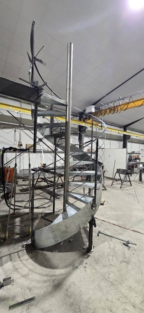 Escalier Colimaçon Métal : Fabrication Sur Mesure en Atelier Escalier en colimaçon en métal en cours de fabrication dans un atelier industriel avec garde-corps soudés.
